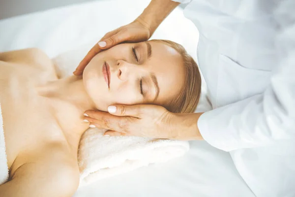 Hermosa mujer feliz disfrutando de masaje facial con los ojos cerrados en el salón de spa. Tratamiento relajante en medicina y concepto de belleza — Foto de Stock