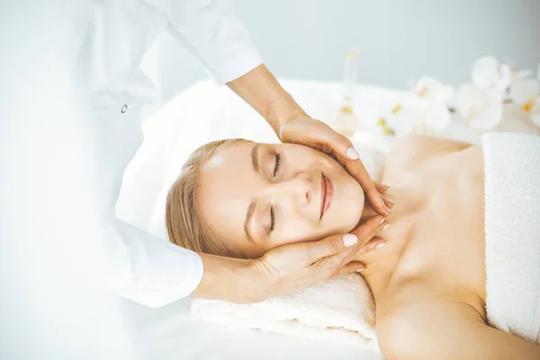 Krásná šťastná žena si užívá masáž obličeje se zavřenýma očima v lázeňském salonu. Relaxační léčba v medicíně a konceptu krásy — Stock fotografie