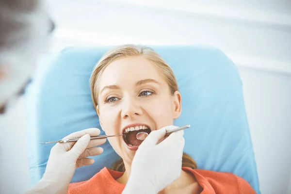 Szczęśliwa uśmiechnięta kobieta jest badana przez dentystę w klinice dentystycznej. Zdrowe zęby i medycyna, koncepcja stomatologii — Zdjęcie stockowe