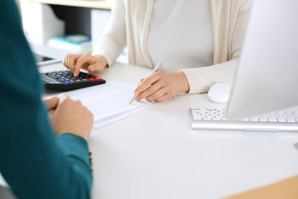 Бухгалтер, проверяющий финансовую отчетность или рассчитывающий с помощью калькулятора доход для налоговой формы, руки крупным планом. Деловая женщина сидит и работает с коллегой за столом в офисе. Концепция аудита