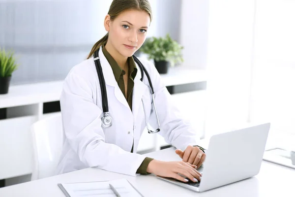 Médico digitando no computador portátil enquanto sentado na mesa no escritório do hospital. Médica no trabalho. Dados em medicina e cuidados de saúde — Fotografia de Stock