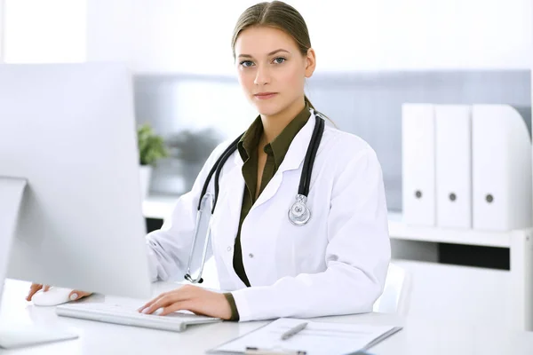 Médico escribiendo en el ordenador PC mientras está sentado en el escritorio en la oficina del hospital. Mujer médica en el trabajo. Datos en medicina y asistencia sanitaria — Foto de Stock