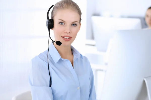 Llama a la oficina central. Hermosa mujer rubia usando computadora y auriculares para consultar a los clientes en línea. Grupo de operadores que trabajan como ocupación de servicio al cliente. Concepto gente de negocios — Foto de Stock