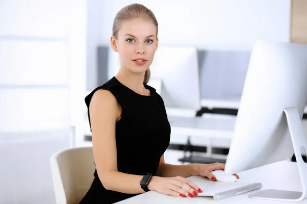 在现代化的办公室里，女商人坐在办公桌前与计算机打交道。秘书或女律师穿黑色衣服看起来很美。商人概念 — 图库照片