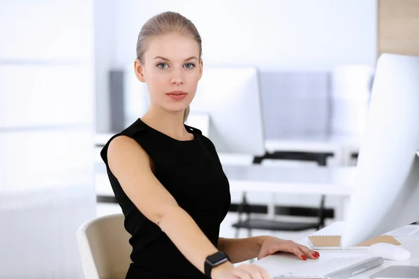 Mulher de negócios trabalhando com computador enquanto sentado na mesa no escritório moderno. Secretária ou advogada fica linda de vestido preto. Conceito de empresários — Fotografia de Stock