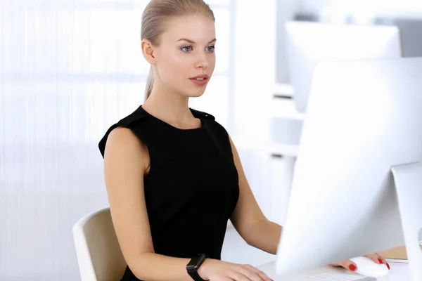 Mujer de negocios que trabaja con la computadora mientras está sentada en el escritorio en la oficina moderna. Secretaria o abogada se ve hermosa en vestido negro. Concepto gente de negocios —  Fotos de Stock