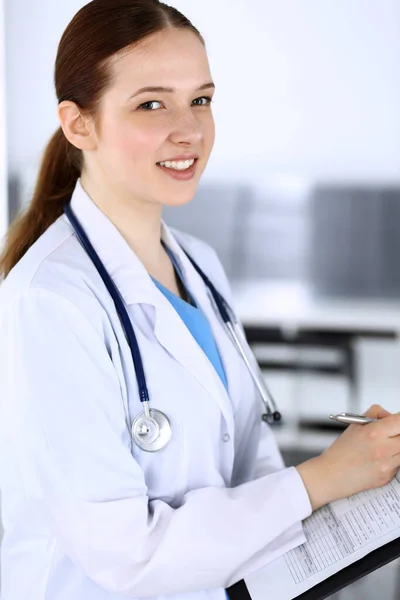 Doctora o estudiante de prácticas en el trabajo. Médico llenando el historial de medicamentos mientras está de pie en la oficina del hospital de emergencia. Concepto de medicina y salud — Foto de Stock