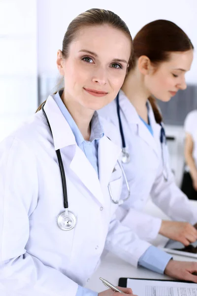 Grupo de médicos en el trabajo en el hospital con el paciente en una cola en el fondo. Médico llenando documentos médicos o receta mientras está de pie en la recepción. Datos en medicina y salud — Foto de Stock