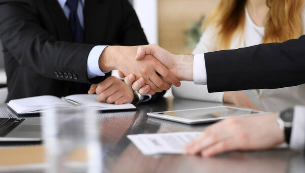 Бизнесмен пожимает руку коллеге или партнеру над стеклянным столом в современном офисе крупным планом. Неизвестные бизнесмены на встрече. Командная работа, партнерство и концепция рукопожатия
