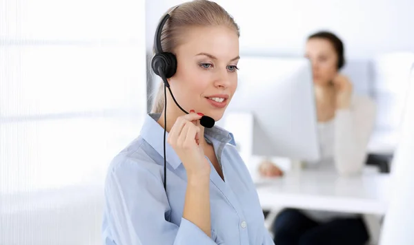 呼叫中心办公室漂亮的金发女人用电脑和耳机在网上咨询客户。作为客户服务职业的操作员群体。商人概念 图库图片