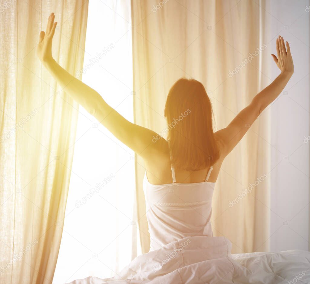 Woman stretching in bed after waking up, back view, entering a day happy and relaxed after good night sleep. Good morning and new day for brunette. Concept of Weekend, holidays