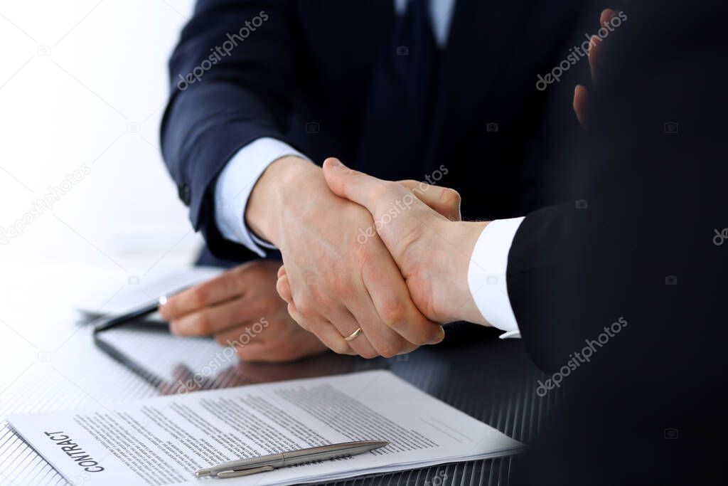 Business people shaking hands after contract signing at the glass desk in modern office. Unknown businessman with colleagues at meeting or negotiation. Teamwork, partnership and handshake concept