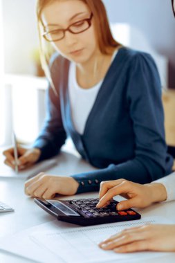Muhasebeci mali durumu kontrol ediyor ya da vergi formları için hesap makinesi geliri ile sayıyor, eller yakın çekim. İş kadını ofisteki masada iş arkadaşıyla oturuyor ve çalışıyor. Denetim kavramı