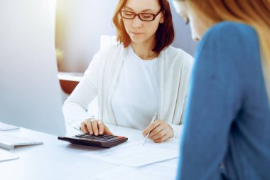 Muhasebeci mali durumu kontrol ediyor ya da vergi formları için hesap makinesi geliri ile sayıyor, eller yakın çekim. İş kadını ofisteki masada iş arkadaşıyla oturuyor ve çalışıyor. Denetim kavramı