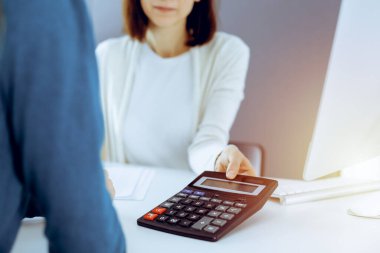 Muhasebeci mali durumu kontrol ediyor ya da vergi formları için hesap makinesi geliri ile sayıyor, eller yakın çekim. İş kadını ofisteki masada iş arkadaşıyla oturuyor ve çalışıyor. Denetim kavramı