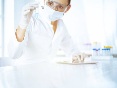 Kadın laboratuvar asistanı mavi sıvıyla test tüpünü analiz ediyor. Tıp, sağlık ve araştırma konsepti