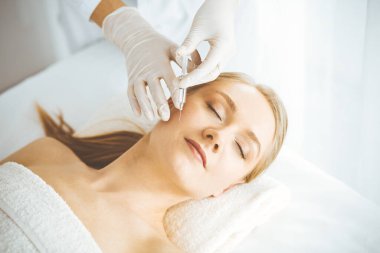 Güzellik doktoru sarışın kadın yüzüne şırıngayla güzellik prosedürü uyguluyor. Kozmetik tıp, güzellik enjeksiyonu konsepti