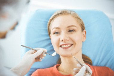 Mutlu gülümseyen kadın dişçi kliniğinde dişçi tarafından muayene ediliyor. Sağlıklı dişler ve ilaçlar, stomatoloji konsepti