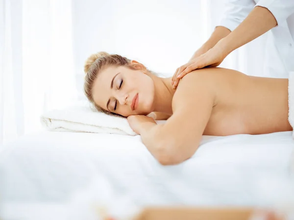 Young and blonde woman enjoying massage of back in spa salon. Beauty concept — Stock Photo, Image