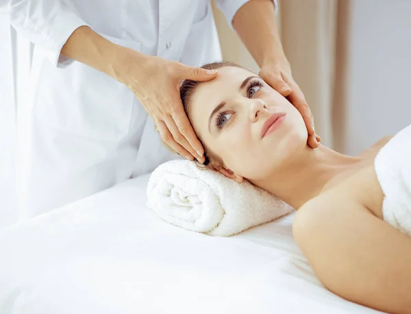 Jonge en blonde vrouw geniet van gezichtsmassage in spa salon. Schoonheidsconcept — Stockfoto