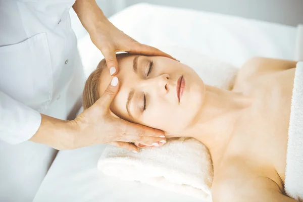 Mooie gelukkige vrouw genieten van gezichtsmassage met gesloten ogen in spa salon. Ontspannende behandeling in de geneeskunde en Beauty concept — Stockfoto