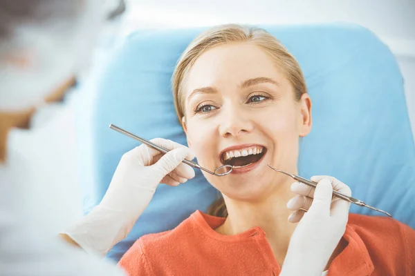 Szczęśliwa uśmiechnięta kobieta jest badana przez dentystę w klinice dentystycznej. Zdrowe zęby i medycyna, koncepcja stomatologii — Zdjęcie stockowe