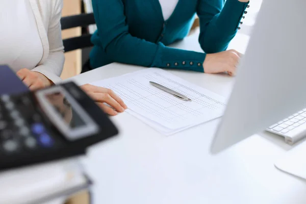 Accountant checking financial statement or counting by calculator income for tax form, hands closeup. Business woman sitting and working with colleague at the desk in office toned in blue. Tax and