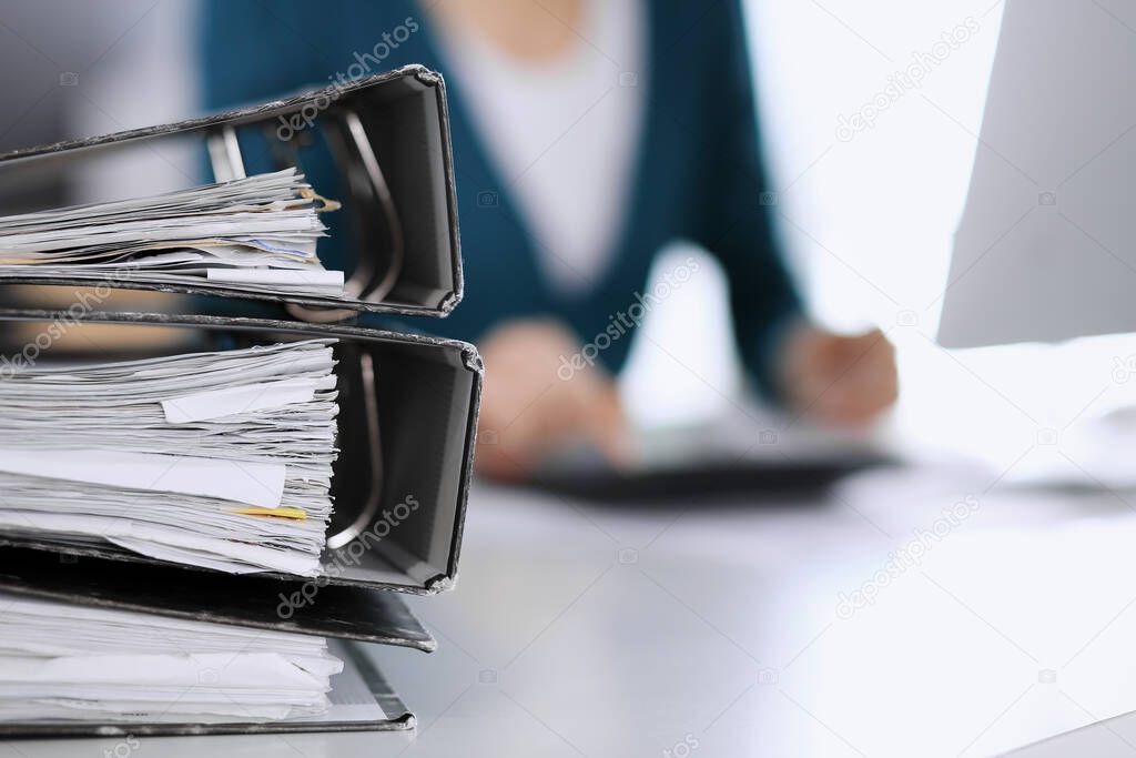 Bnders with papers are waiting to be processed by business woman or bookkeeper working at the desk in office back in blur. Internal Tax and Audit concept