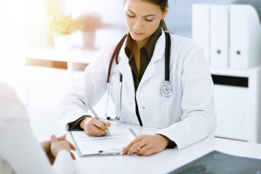 Kadın-doktor ve hasta güneşli hastane ofisinde oturup konuşuyorlar. Yeşil renkli bluz terapiste yakışır. Tıp konsepti