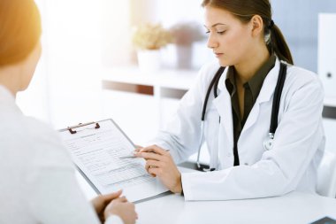 Kadın-doktor ve hasta güneşli hastane ofisinde oturup konuşuyorlar. Yeşil renkli bluz terapiste yakışır. Tıp konsepti