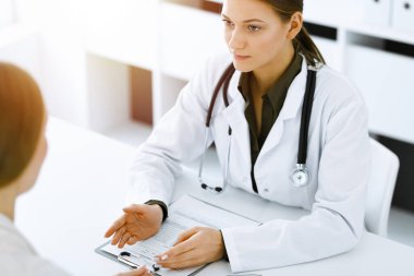 Kadın-doktor ve hasta güneşli hastane ofisinde oturup konuşuyorlar. Yeşil renkli bluz terapiste yakışır. Tıp konsepti