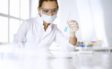 Kadın laboratuvar asistanı mavi sıvıyla test tüpünü analiz ediyor. Tıp, sağlık ve araştırma konsepti