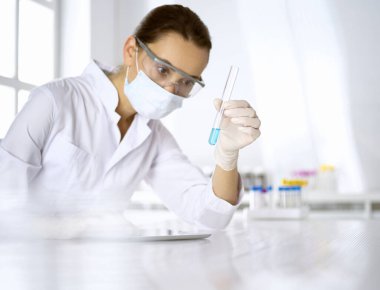 Kadın laboratuvar asistanı mavi sıvıyla test tüpünü analiz ediyor. Tıp, sağlık ve araştırma konsepti