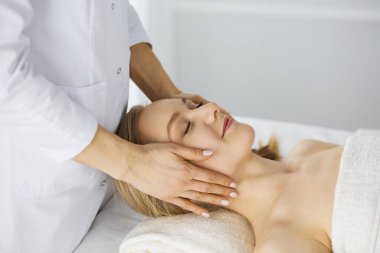 Güzel beyaz kadın spa salonunda gözleri kapalı yüz masajından zevk alıyor. Tıp ve Güzellik konseptinde rahatlatıcı tedavi
