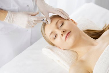 Güzellik doktoru, beyaz kadın yüzüne şırıngayla güzellik prosedürü uyguluyor. Kozmetik tıp ve cerrahi, güzellik enjeksiyonları konsepti