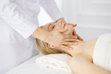 Güzel beyaz kadın spa salonunda gözleri kapalı yüz masajından zevk alıyor. Tıp ve Güzellik konseptinde rahatlatıcı tedavi