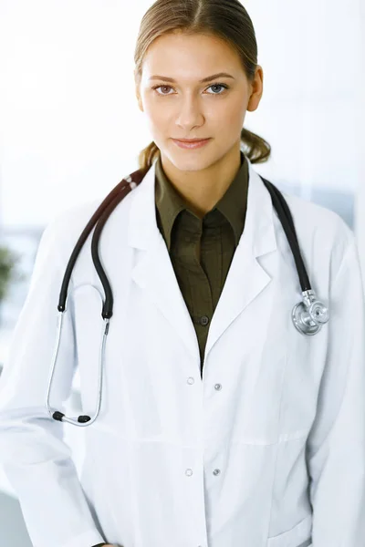 Mujer-médico de pie y mirando a la cámara en la clínica soleada. Un servicio médico perfecto. Medicina y asistencia sanitaria — Foto de Stock