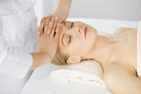 Piękna biała kobieta ciesząca się masażem twarzy z zamkniętymi oczami w salonie spa. Leczenie relaksacyjne w medycynie i koncepcji piękna — Zdjęcie stockowe
