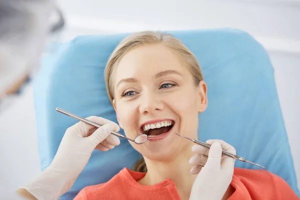 Uśmiechnięta biała kobieta jest badana przez dentystę w klinice stomatologicznej. Zdrowe zęby i medycyna, koncepcja stomatologii — Zdjęcie stockowe