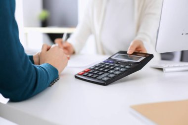 Mali durumu kontrol eden ya da vergi formları için hesap makinesinin geliri ile sayan, elleri yakın çekim. İş kadını ofisteki masada iş arkadaşıyla oturuyor ve çalışıyor. Vergi ve Denetim kavramı