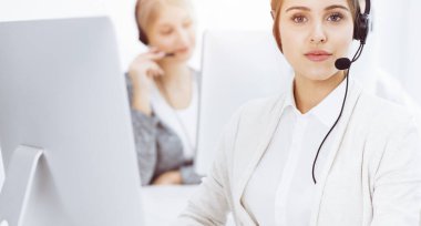 Güneşli ofiste çağrı merkezi. Çeşitli operatörler iş başında. Telepazarlama servisinin müşterileriyle iletişim kuran kulaklıklı güzel bir kadın. İş konsepti