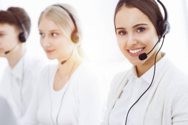 Güneşli ofiste çağrı merkezi. Çeşitli operatörler iş başında. Telepazarlama servisinin müşterileriyle iletişim kuran kulaklıklı güzel bir kadın. İş konsepti