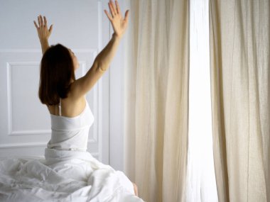 Bir kadın uyandıktan sonra yatakta geriniyor, geriye bakıyor, bir güne mutlu ve rahat giriyor iyi bir gece uykusundan sonra. Esmer için günaydın ve yeni bir gün. Hafta sonu kavramı, tatiller