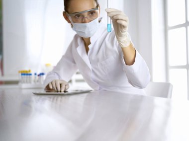Kadın laboratuvar asistanı mavi sıvıyla test tüpünü analiz ediyor. Tıp, sağlık ve araştırma konsepti