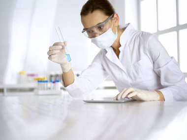 Kadın laboratuvar asistanı mavi sıvıyla test tüpünü analiz ediyor. Tıp, sağlık ve araştırma konsepti