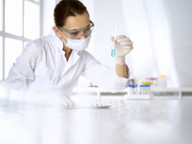 Kadın laboratuvar asistanı mavi sıvıyla test tüpünü analiz ediyor. Tıp, sağlık ve araştırma konsepti