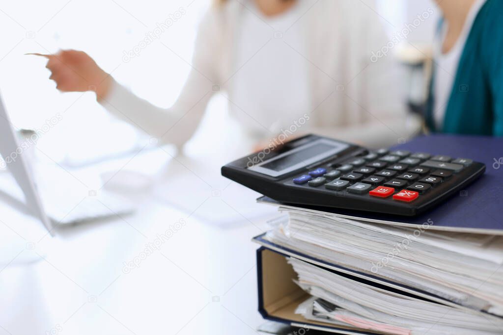 Calculator and binders with papers are waiting to be processed by business woman or bookkeeper working at the desk in office back in blur. Internal Audit and tax concept