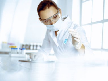 Kadın laboratuvar asistanı mavi sıvıyla test tüpünü analiz ediyor. Tıp, sağlık ve araştırma konsepti