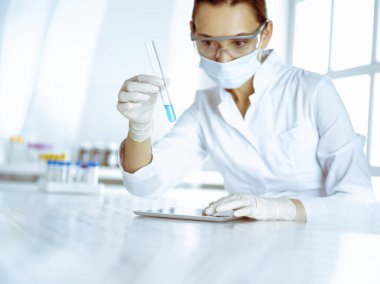 Kadın laboratuvar asistanı mavi sıvıyla test tüpünü analiz ediyor. Tıp, sağlık ve araştırma konsepti