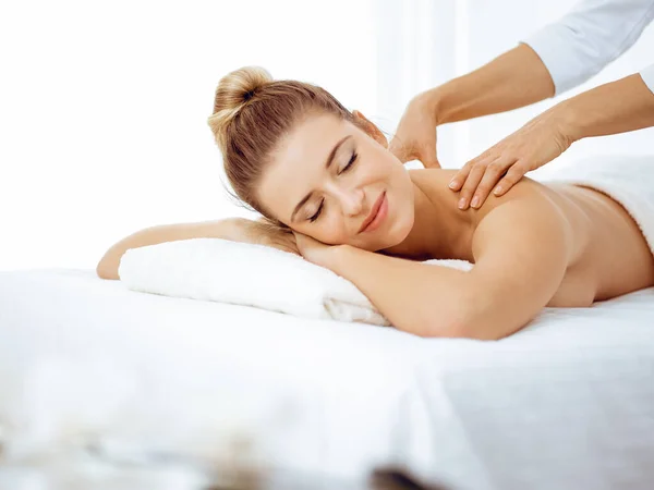 Young and blonde woman enjoying massage of back in spa salon. Beauty concept — Stock Photo, Image